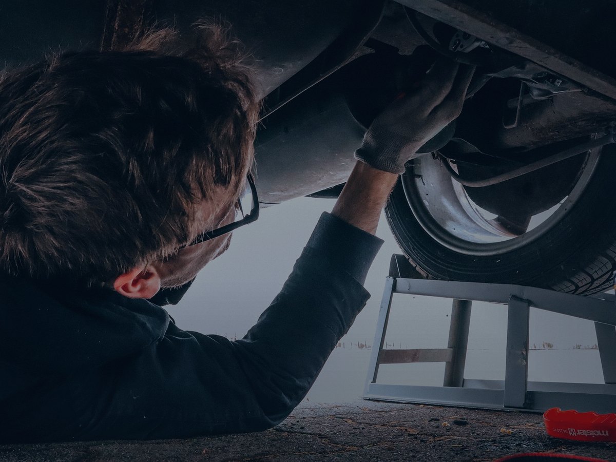Mechanic lying under a vehicle on ramps carrying out a repair